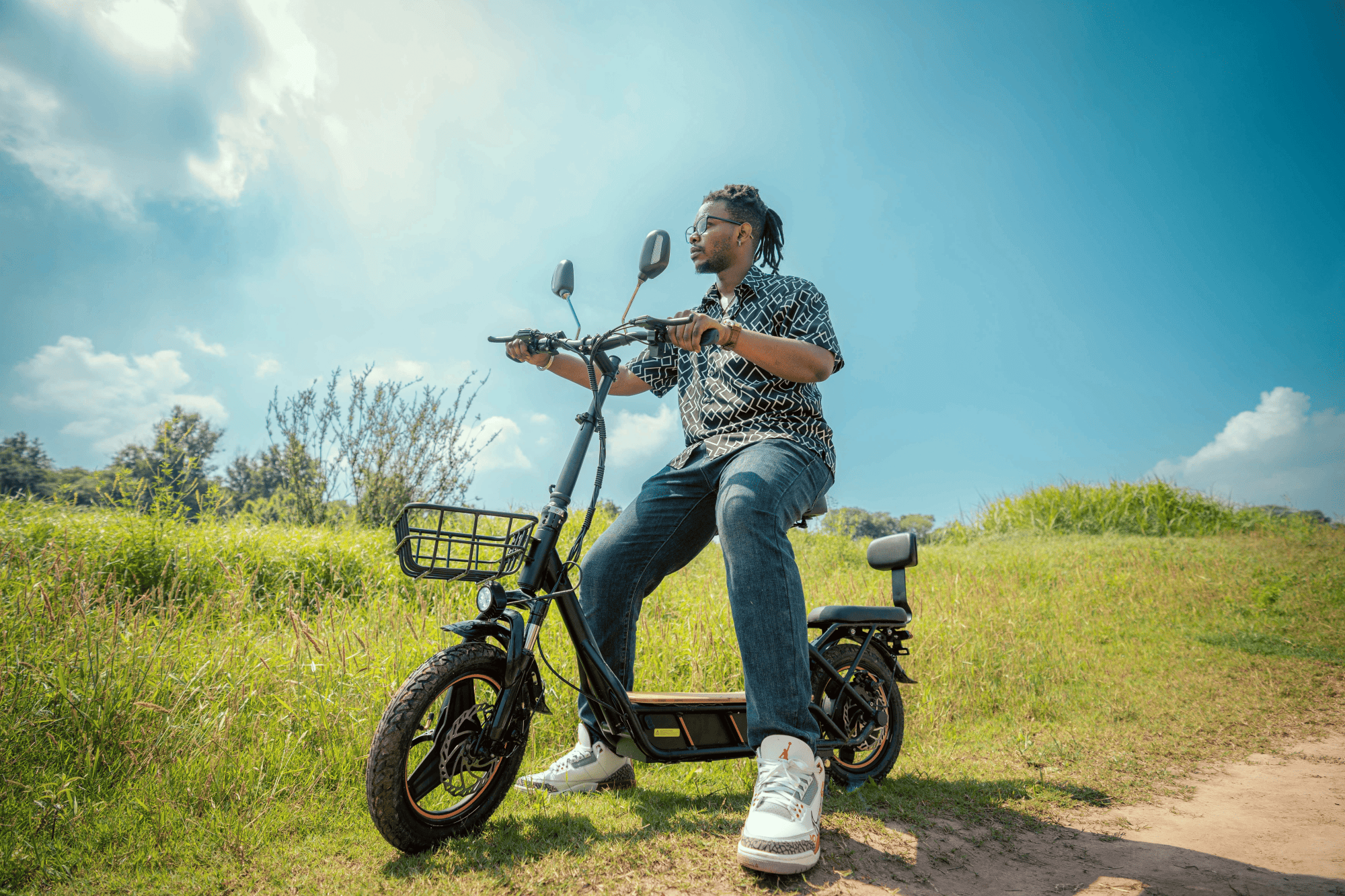 Man sitting on an kukirin c1 pro electric bike in a grassy field with a clear blue sky.